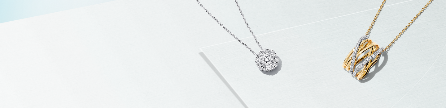 Birks Ros&eacute;e du Matin Diamond and Yellow Gold Pendant and Birks Snowflake Diamond Pendant on a blue background.